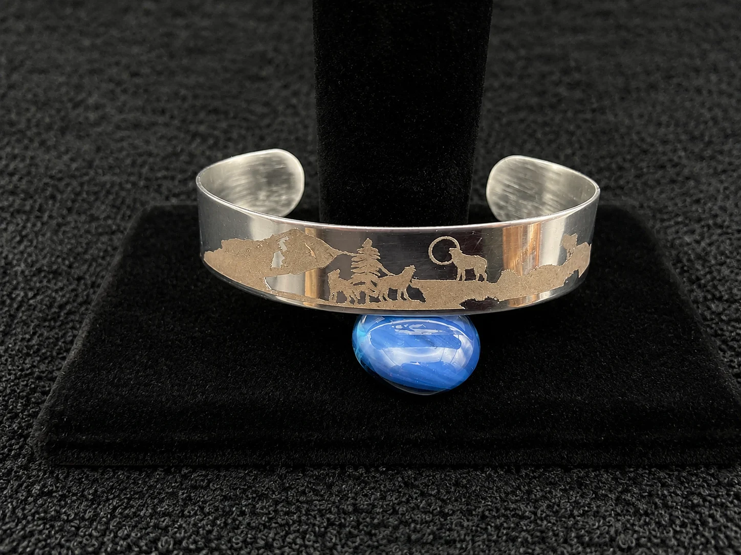 Stainless steel wolf bracelet displayed on a black stand